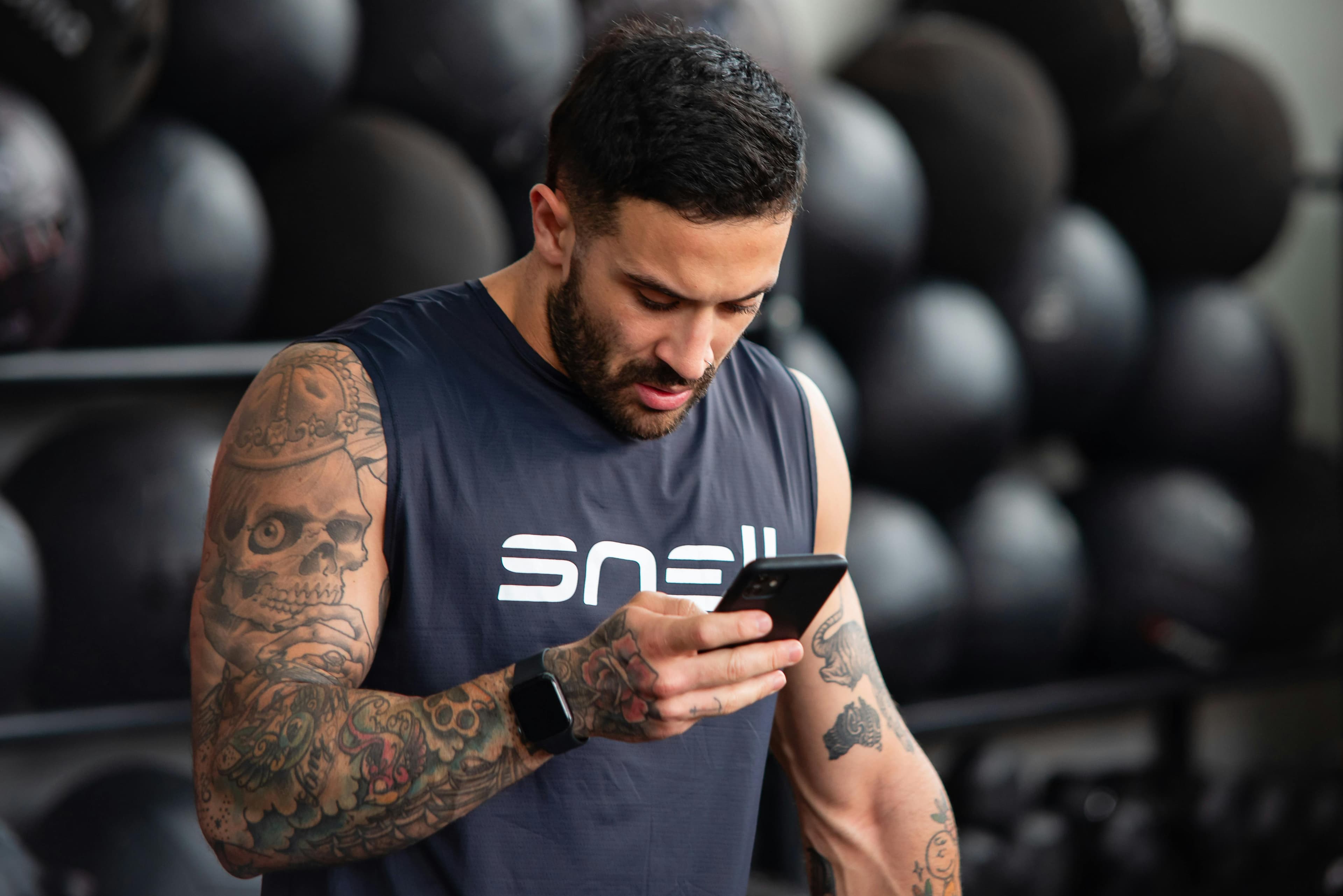 Muscular athlete reviewing performance data on a smartphone between sets